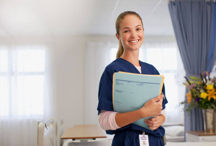 Medical assistant standing with patient paperwork in hands, smiling in a hospital setting