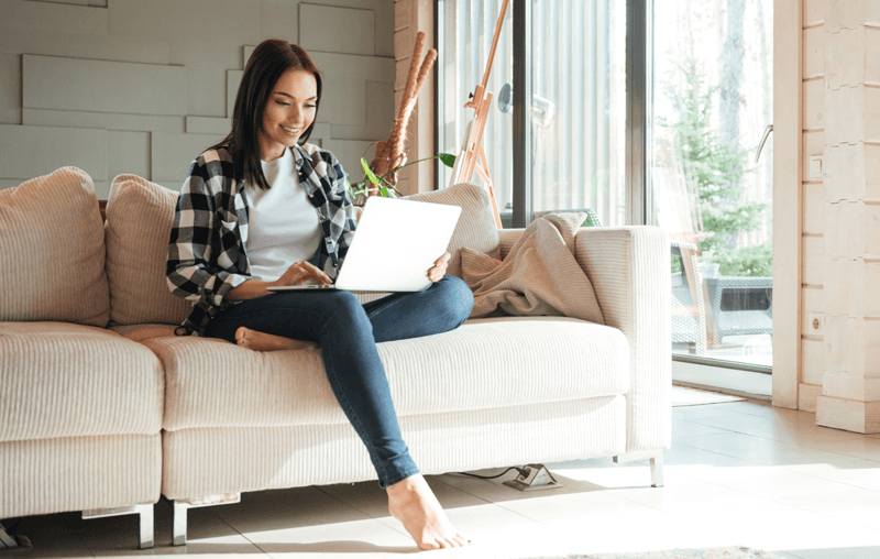 A student sitting on the couch taking online courses.