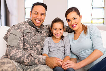 military family, husband in uniform with wife and daughter smiling while sitting on couch