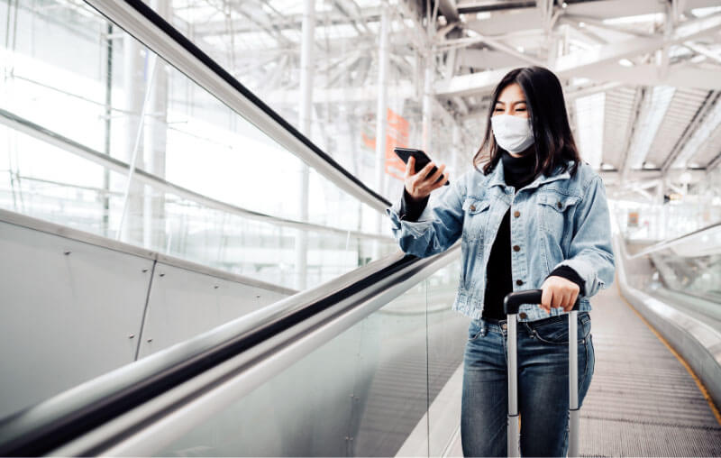 woman going down escalator with her phone and mask on