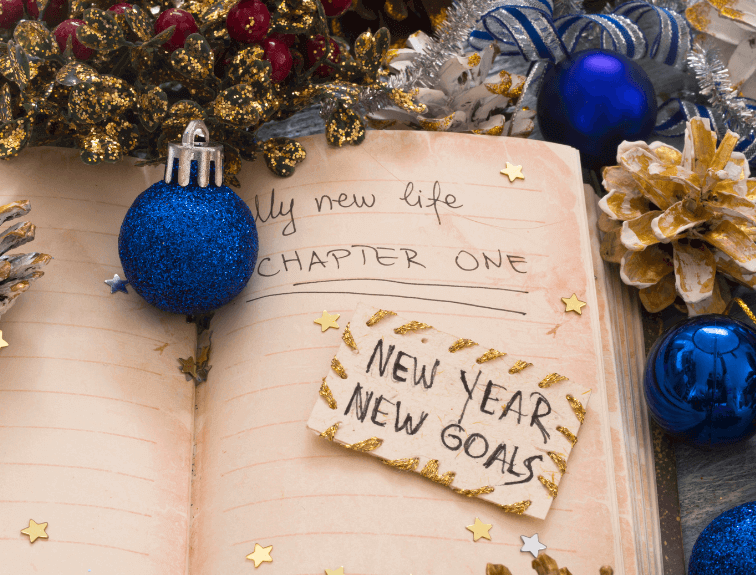 Image of journal that is surrounded by blue and gold ornaments with writing "My new life - Chapter One" in it and card stating "New Year, New Goals" on top