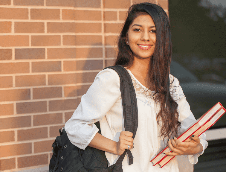 Image of International Student with black backpack on shoulder and holding textbooks